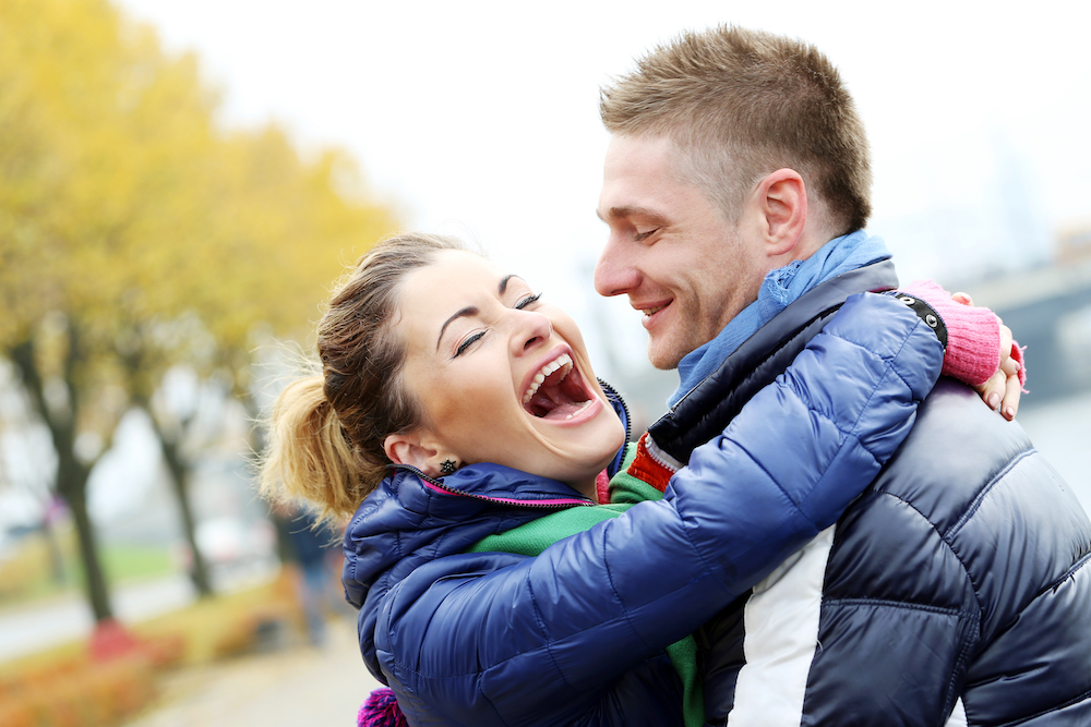 femme qui rit qui se jette au cou de son compagnon souriant