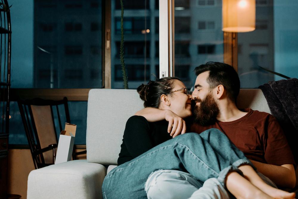 Couple complice assis sur un canapé qui sont nez à nez et souriants